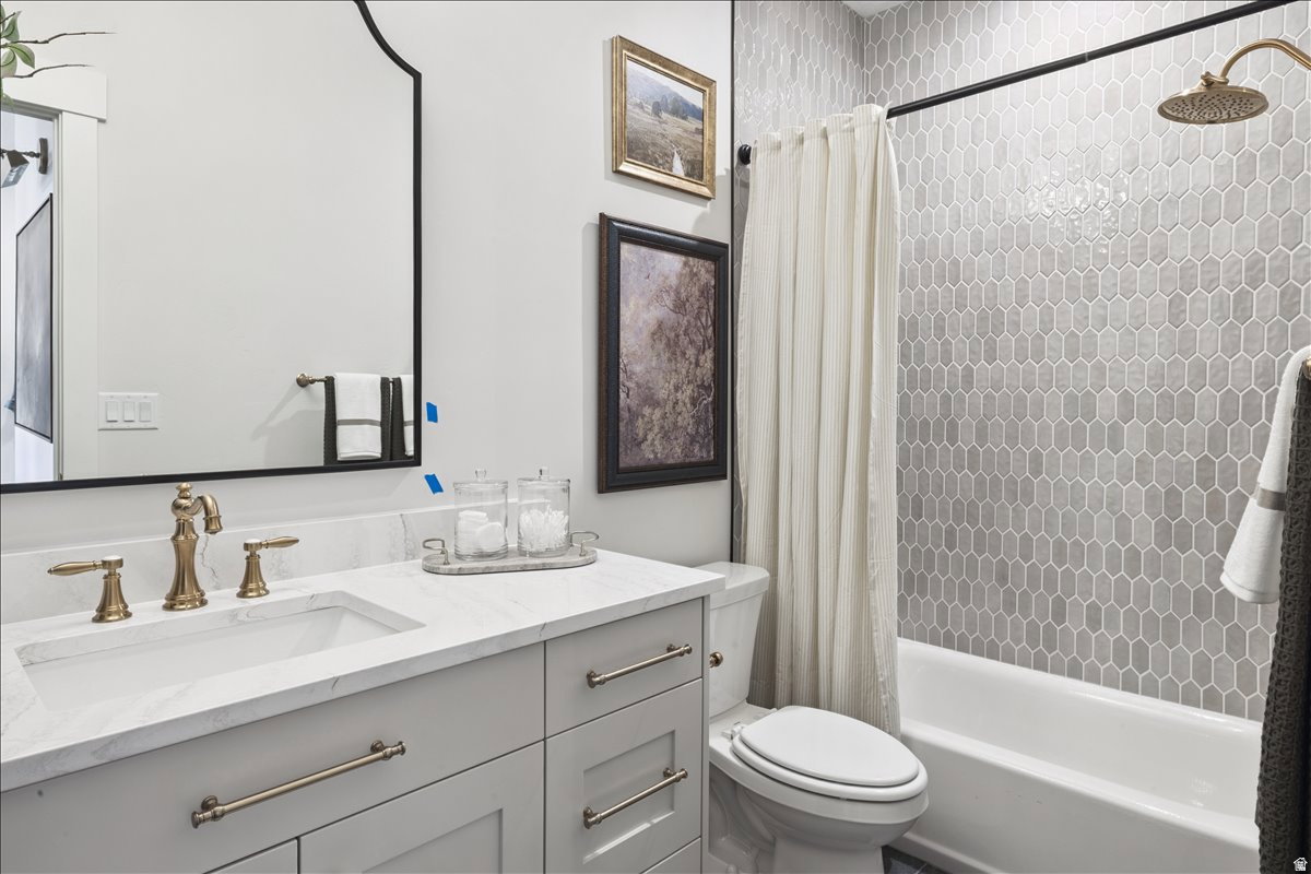 Bathroom featuring a vanity with a white countertop and undermount sink, brushed brass hardware, a black-framed mirror, and a tiled shower with a white tub