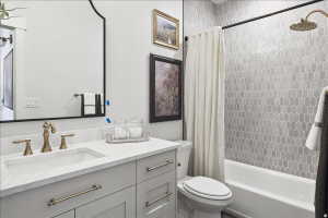 Bathroom featuring a vanity with a white countertop and undermount sink, brushed brass hardware, a black-framed mirror, and a tiled shower with a white tub