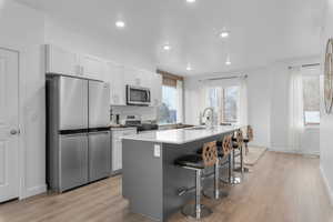 Two tone kitchen featuring stainless steel appliances, a center island with sink, light wood-style floors, a breakfast bar, and recessed lighting
