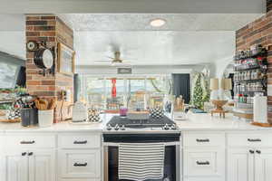 Kitchen featuring stainless steel gas range oven, light stone counters, a textured ceiling, tasteful backsplash, and white cabinetry