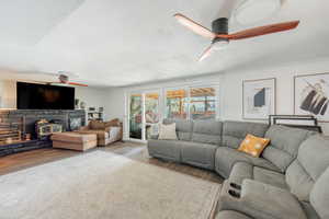 Living room featuring ceiling fan, wood finished floors, a textured ceiling, ornamental molding, and a wood stove