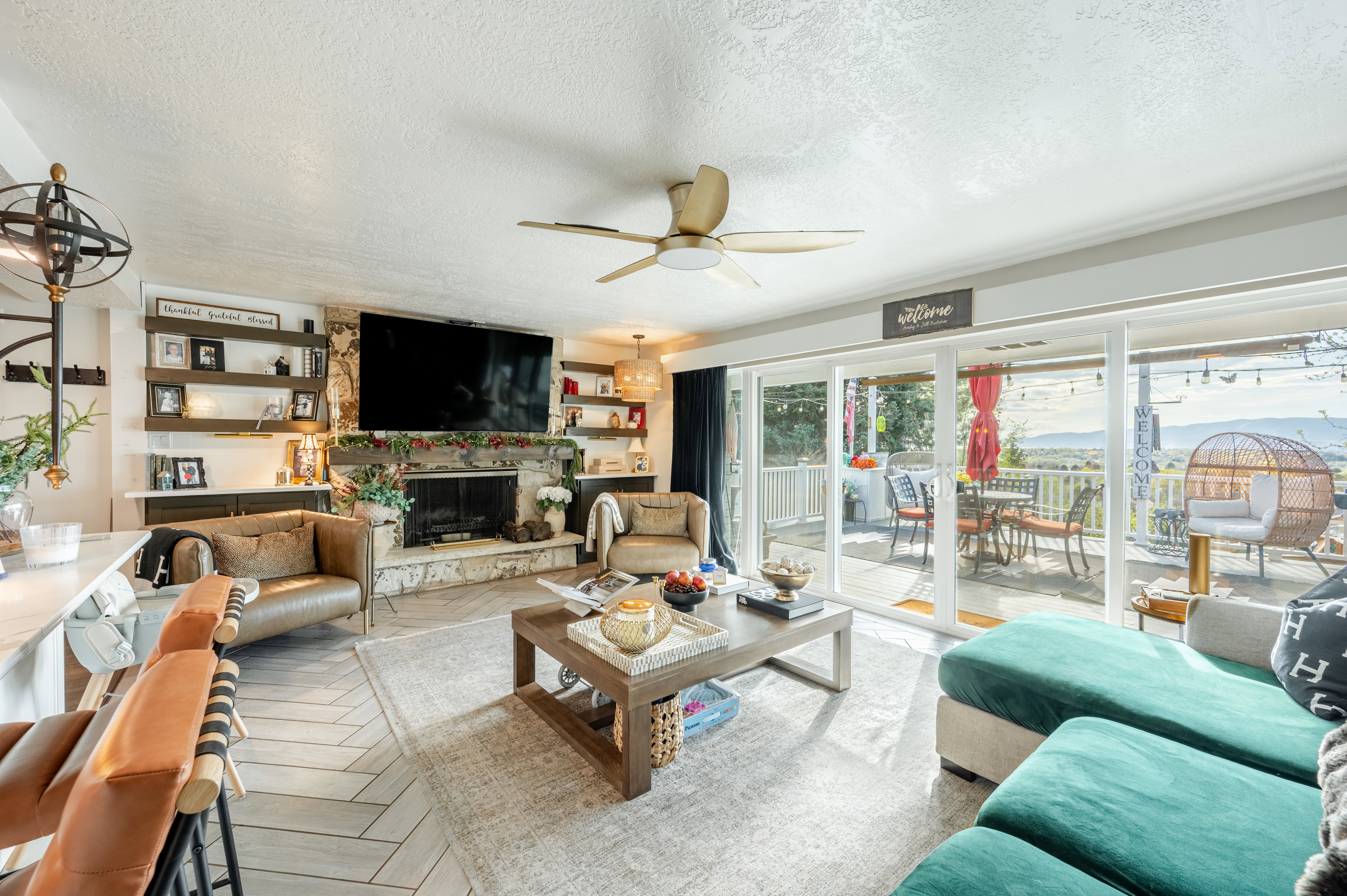 Living room featuring a textured ceiling, ceiling fan, a stone fireplace, and parquet flooring