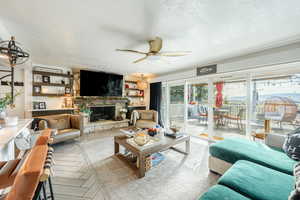 Living room featuring a textured ceiling, ceiling fan, a stone fireplace, and parquet flooring