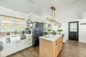 Kitchen featuring freestanding refrigerator, two tone cabinetry, dark wood-style floors, a center island, and ornamental molding
