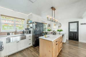 Dual tone kitchen with freestanding refrigerator, dual tone cabinets, dark wood finished floors, crown molding, and a kitchen island