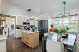 Dual tone kitchen with freestanding refrigerator, a kitchen island, crown molding, dark wood-style flooring, and a textured ceiling