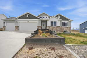 Craftsman-style home with stone siding, a garage, concrete driveway, board and batten siding, and a front lawn