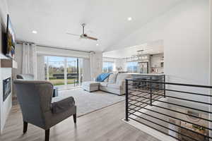 Living area with lofted ceiling, light wood-type flooring, ceiling fan, recessed lighting, and a fireplace