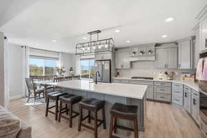 Kitchen with gray cabinetry, a breakfast bar, an island with sink, stainless steel appliances, and light wood-style floors