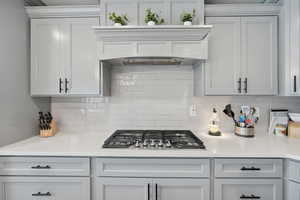 Kitchen featuring light stone counter tops, stainless steel gas stove top, and tile back splash