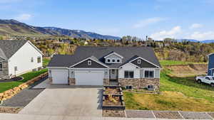 Craftsman-style home featuring an attached garage, stone siding, a mountain view, driveway, and a front lawn