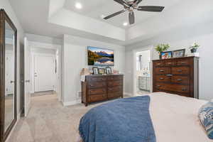 Bedroom featuring recessed lighting, light carpet, a tray ceiling, ceiling fan, and ensuite bath