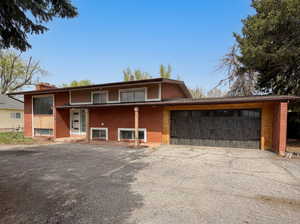 Split foyer home featuring brick siding, a garage, driveway, and a chimney