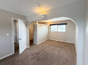 Unfurnished bedroom with arched walkways and dark colored carpet