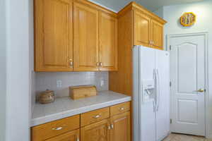 Kitchen with white fridge with ice dispenser, decorative backsplash, wood finish cabinets, tile counters, and light tile patterned flooring