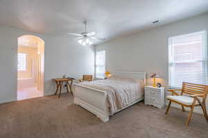 Bedroom featuring arched walkways, light carpet, ensuite bath, a ceiling fan, and a textured ceiling