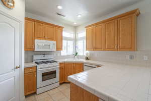 Kitchen featuring white appliances, tile counters, light tile patterned floors, tasteful backsplash, and recessed lighting