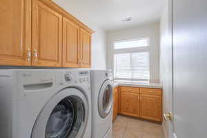 Laundry area with washing machine and clothes dryer, light tile patterned floors, and cabinet space