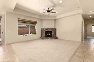 Unfurnished living room featuring a raised ceiling, ceiling fan, light tile patterned floors, recessed lighting, and a stone fireplace