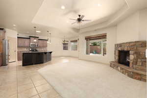 Unfurnished living room with ceiling fan, recessed lighting, a stone fireplace, light tile patterned flooring, and a tray ceiling