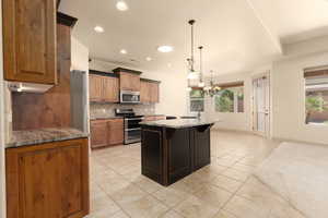Kitchen featuring dark stone countertops, stainless steel appliances, wood finish cabinets, light tile patterned flooring, and decorative backsplash