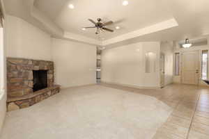 Unfurnished living room with a stone fireplace, a raised ceiling, a ceiling fan, recessed lighting, and light tile patterned floors