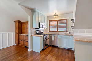 Kitchen with stainless steel appliances, dark wood-style floors, a decorative wall, tasteful backsplash, and wainscoting