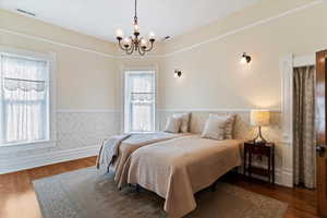 Bedroom with wainscoting, suspended lighting, and dark wood-type flooring