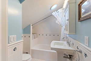 Bathroom with lofted ceiling, wainscoting, shower / bath combination with curtain, tile walls, and light tile patterned flooring