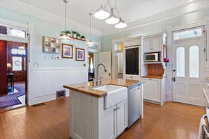 Kitchen featuring plenty of natural light, white cabinetry, a center island with sink, light stone counters, and a wainscoted wall