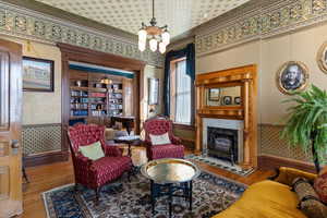 Living area featuring wallpapered walls, wood finished floors, hanging lights, and a fireplace with raised hearth