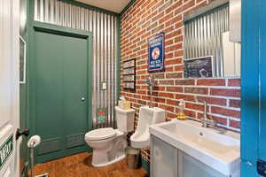 Half bathroom featuring vanity, brick wall, and dark wood-type flooring
