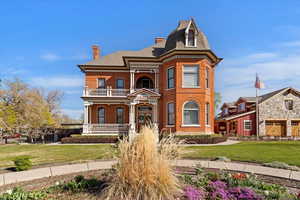 View of front of property featuring a front yard, brick siding, a chimney, covered porch, and a shingled roof