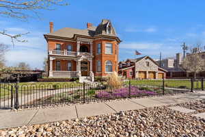 Victorian house with brick siding, a chimney, a porch, and a fenced front yard