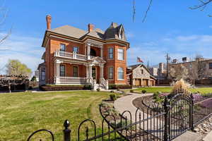 Victorian-style house featuring a chimney, a fenced front yard, brick siding, a porch, and a gate
