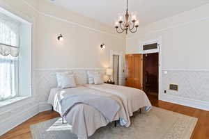 Bedroom featuring wood finished floors, wallpapered walls, suspended lighting, and wainscoting