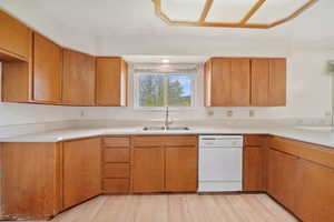 Kitchen featuring white dishwasher, light wood finished floors, wood finish cabinets, and light countertops