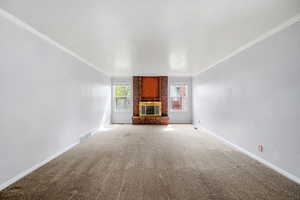 Unfurnished living room featuring carpet, a brick fireplace, and ornamental molding