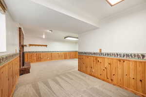 Finished basement featuring wainscoting, wooden walls, crown molding, and light carpet