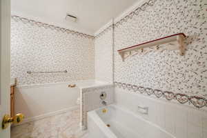Full bathroom featuring a wainscoted wall, vanity, ornamental molding, a garden tub, and wallpapered walls