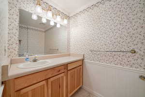 Bathroom with wallpapered walls, a wainscoted wall, crown molding, and vanity