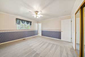 Unfurnished bedroom featuring wallpapered walls, ornamental molding, a textured ceiling, light carpet, and a ceiling fan