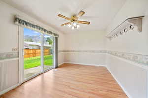 Empty room with wallpapered walls, a ceiling fan, light wood-style flooring, a mountain view, and wainscoting