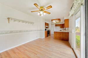 Kitchen featuring wood finish cabinets, wainscoting, light countertops, light wood-style floors, and electric stove