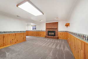 Unfurnished living room featuring a wainscoted wall, wood walls, a brick fireplace, crown molding, and light colored carpet