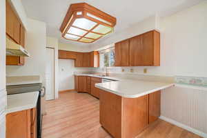 Kitchen with black electric range, wood finish cabinets, a peninsula, and light countertops