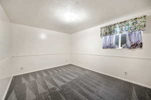 Empty room with a textured ceiling and dark carpet