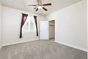 Unfurnished bedroom with a walk in closet, light colored carpet, and ceiling fan