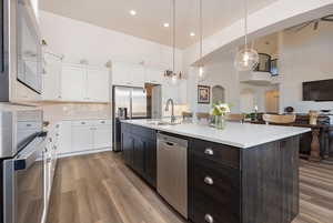Kitchen with two tone cabinetry, a high ceiling, a center island with sink, stainless steel appliances, and decorative backsplash