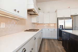 Kitchen with stainless steel appliances, dark wood finished floors, dual tone cabinets, light stone countertops, and decorative backsplash